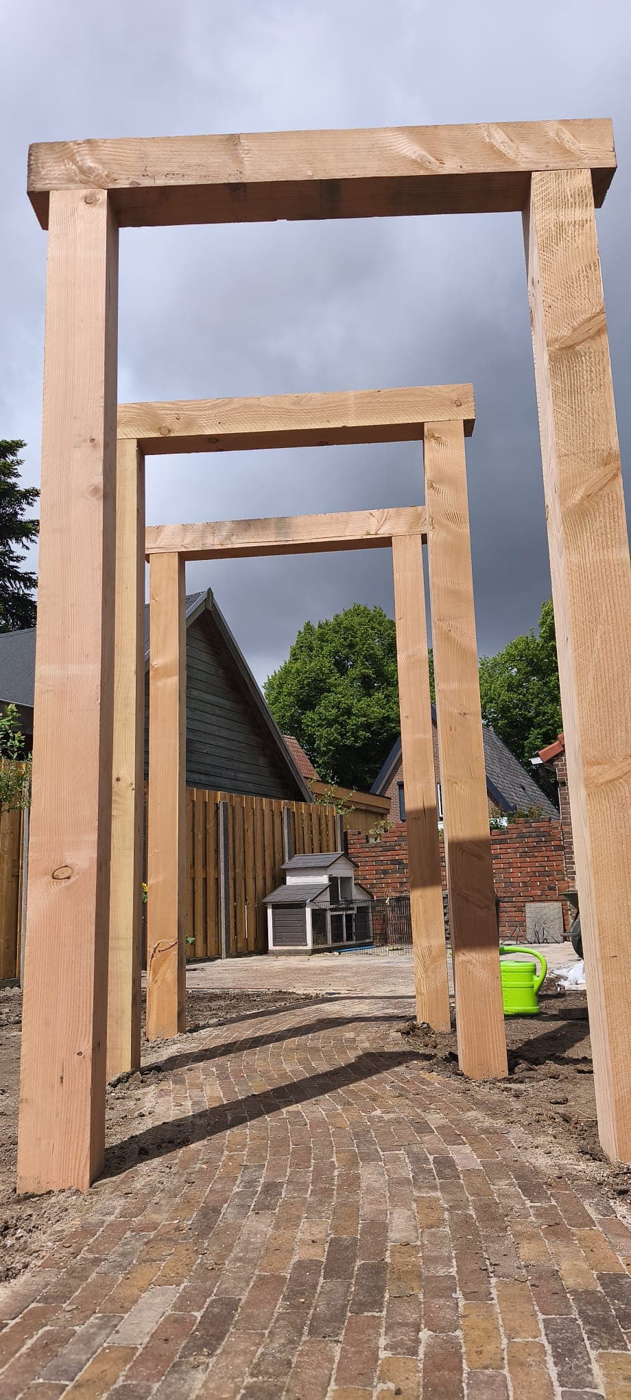 Three Douglas fir pergola portals over a curved clinker path against a storm sky