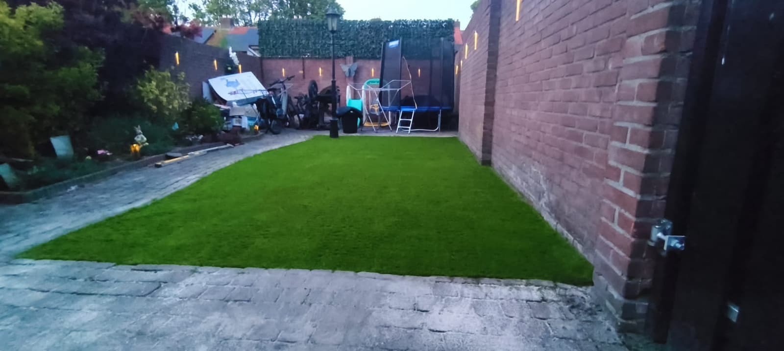 Completed artificial lawn framed by brick walls with lit sconces at dusk